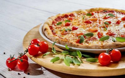 Pizza aux tomates et feuilles vertes sur un plateau de bois avec tomates cerises et poivrons