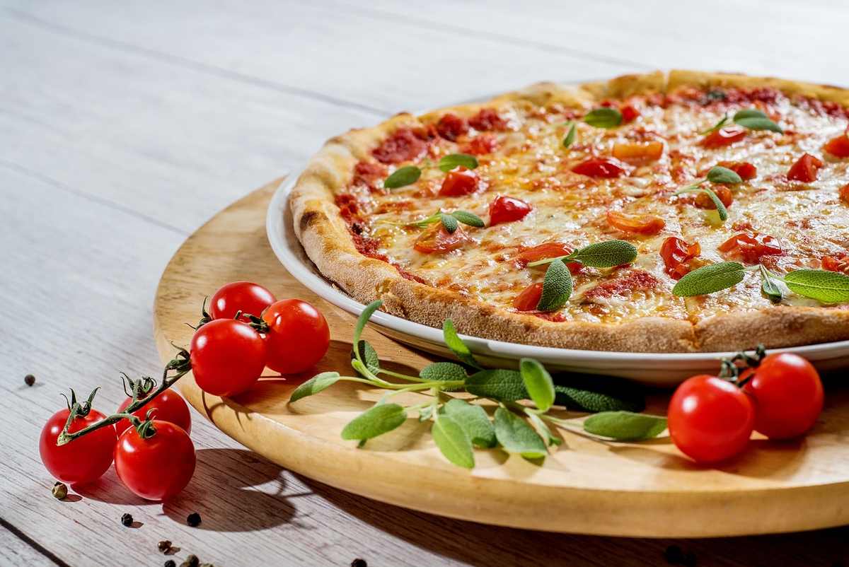 Pizza aux tomates et feuilles vertes sur un plateau de bois avec tomates cerises et poivrons